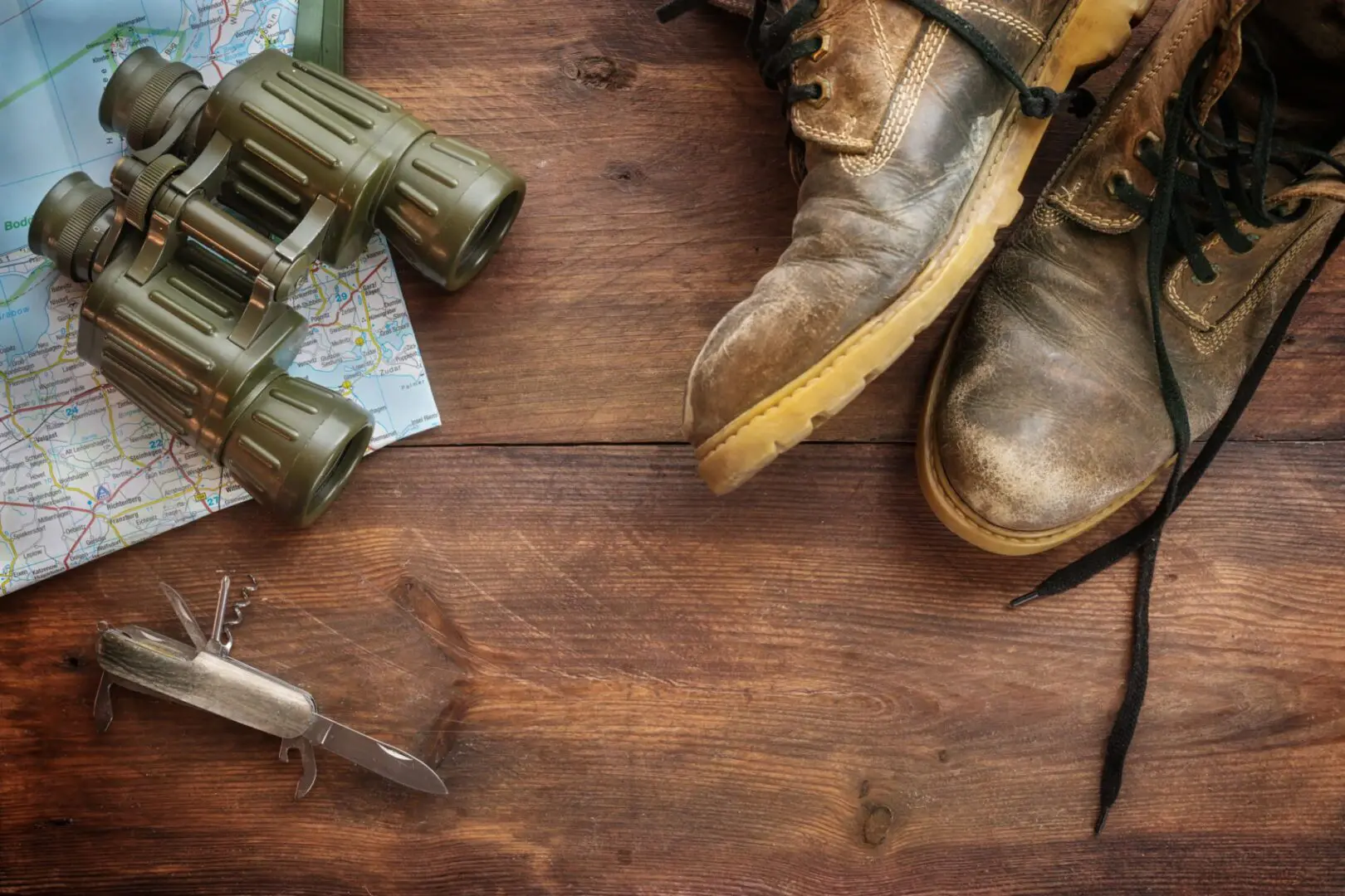 Map, binoculars, boots, and knife on wood.