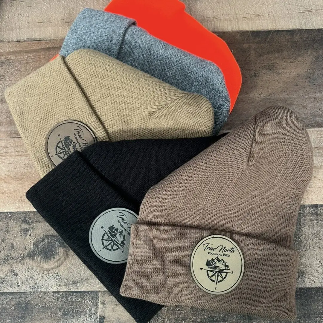 Four folded beanies in gray, red, black, and brown with round patches.