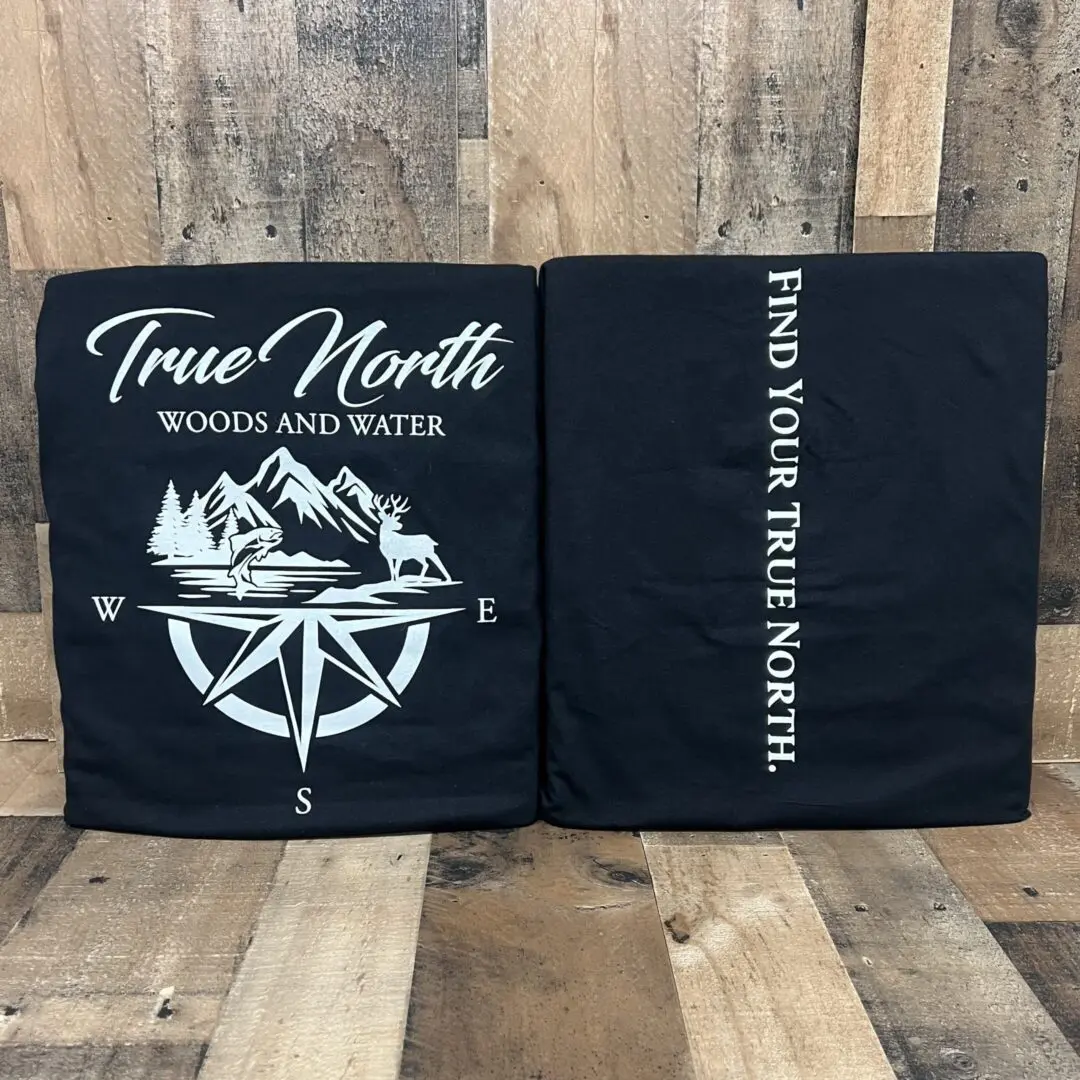 Two black T-shirts with mountain and compass designs.