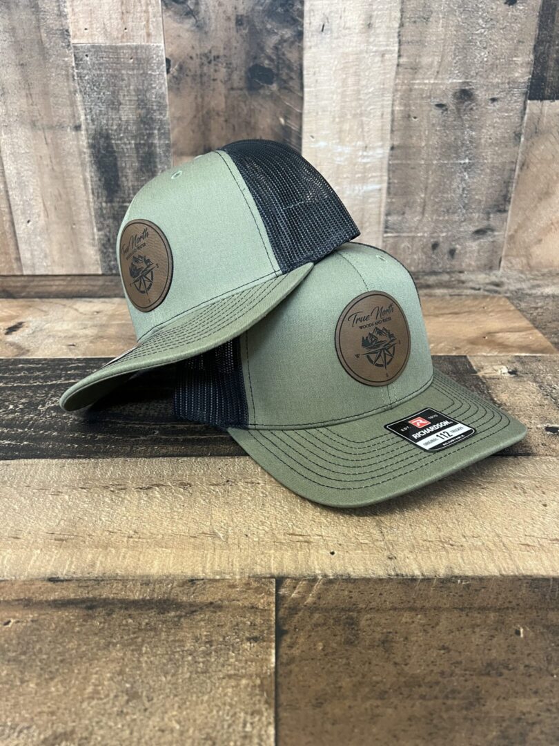 Two green and black baseball caps with round leather patches on the front.