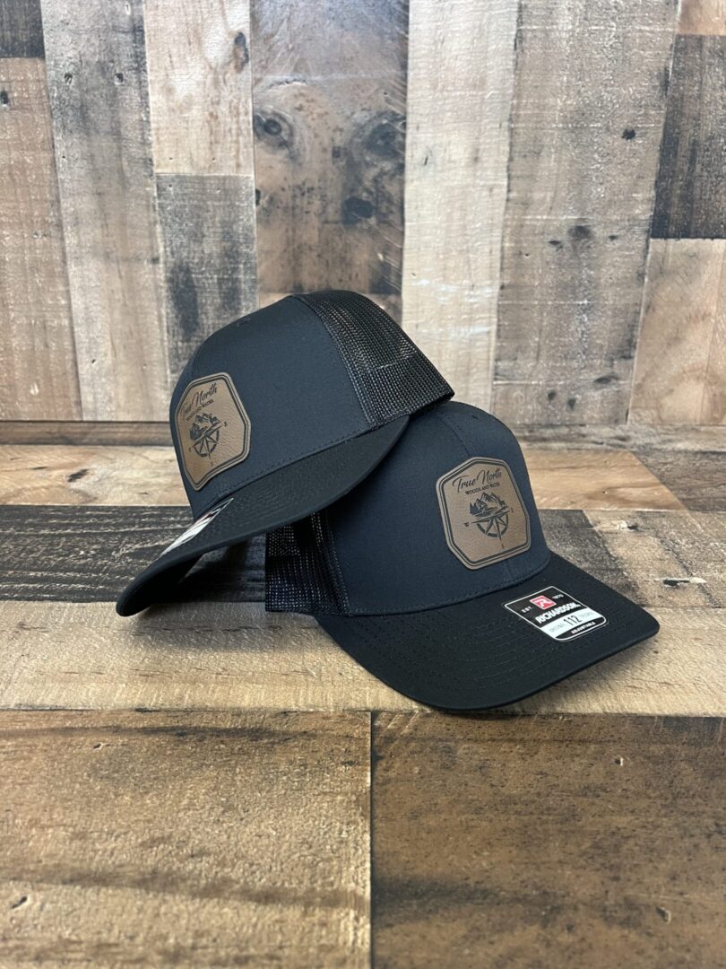 Two black mesh baseball caps with patches on a wooden surface.